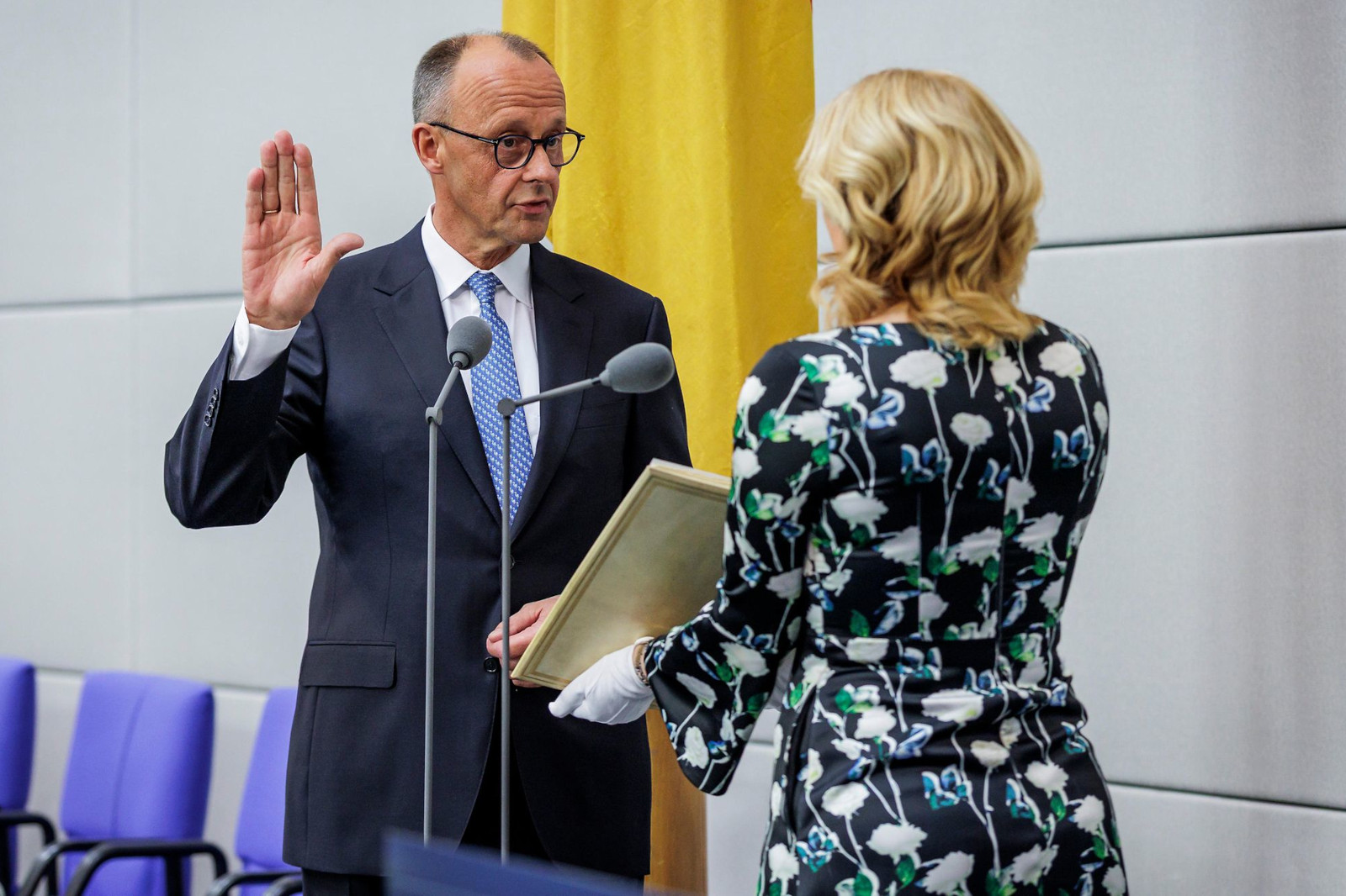 Eine Person legt einen Eid ab, während sie ein Buch hält. Eine andere Person in formeller Kleidung beobachtet die Zeremonie.