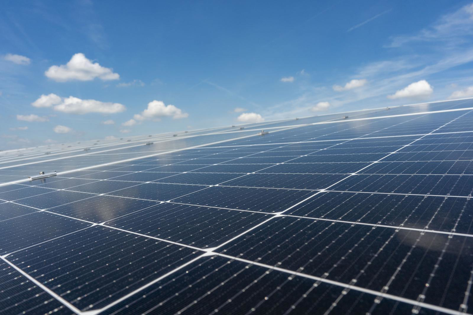 Eine Nahaufnahme von Solarpanelen mit einem klaren blauen Himmel und fluffigen Wolken im Hintergrund.