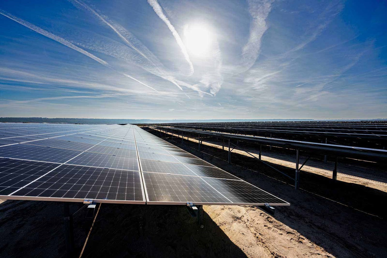 Eine Solaranlage mit Reihen von Solarpanels unter einem hellen Himmel, Sonnenlicht reflektiert sich auf den Panels.