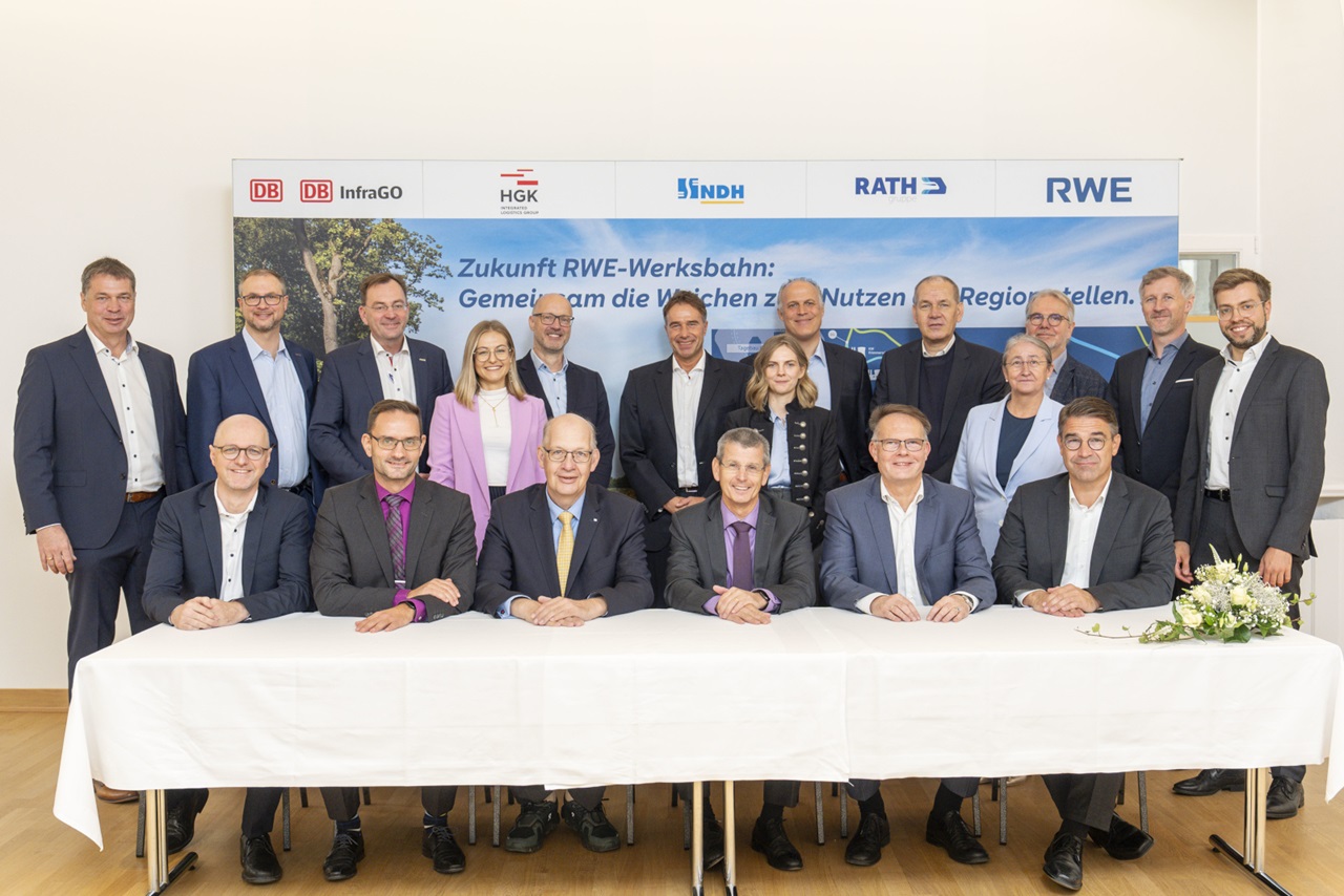 Eine Gruppe von Fachleuten sitzt um einen Tisch, mit einem Hintergrund, der den Text über die Zukunft der RWE-Werksbahn zeigt.
