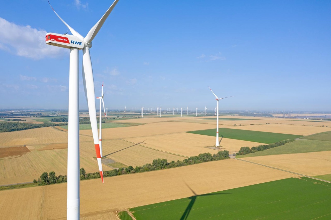 Luftansicht von Windturbinen auf goldenen Feldern, unter einem klaren blauen Himmel, der die Erzeugung erneuerbarer Energie zeigt.