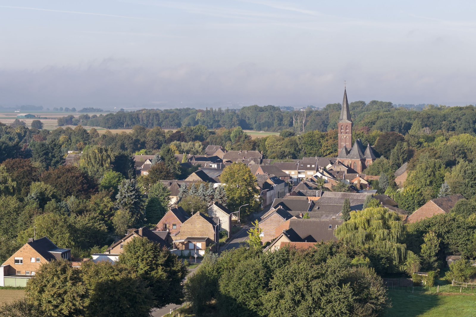 Eine malerische Dorflandschaft mit traditionellen Häusern, einem Kirchturm und üppigem Grün unter einem klaren Himmel.