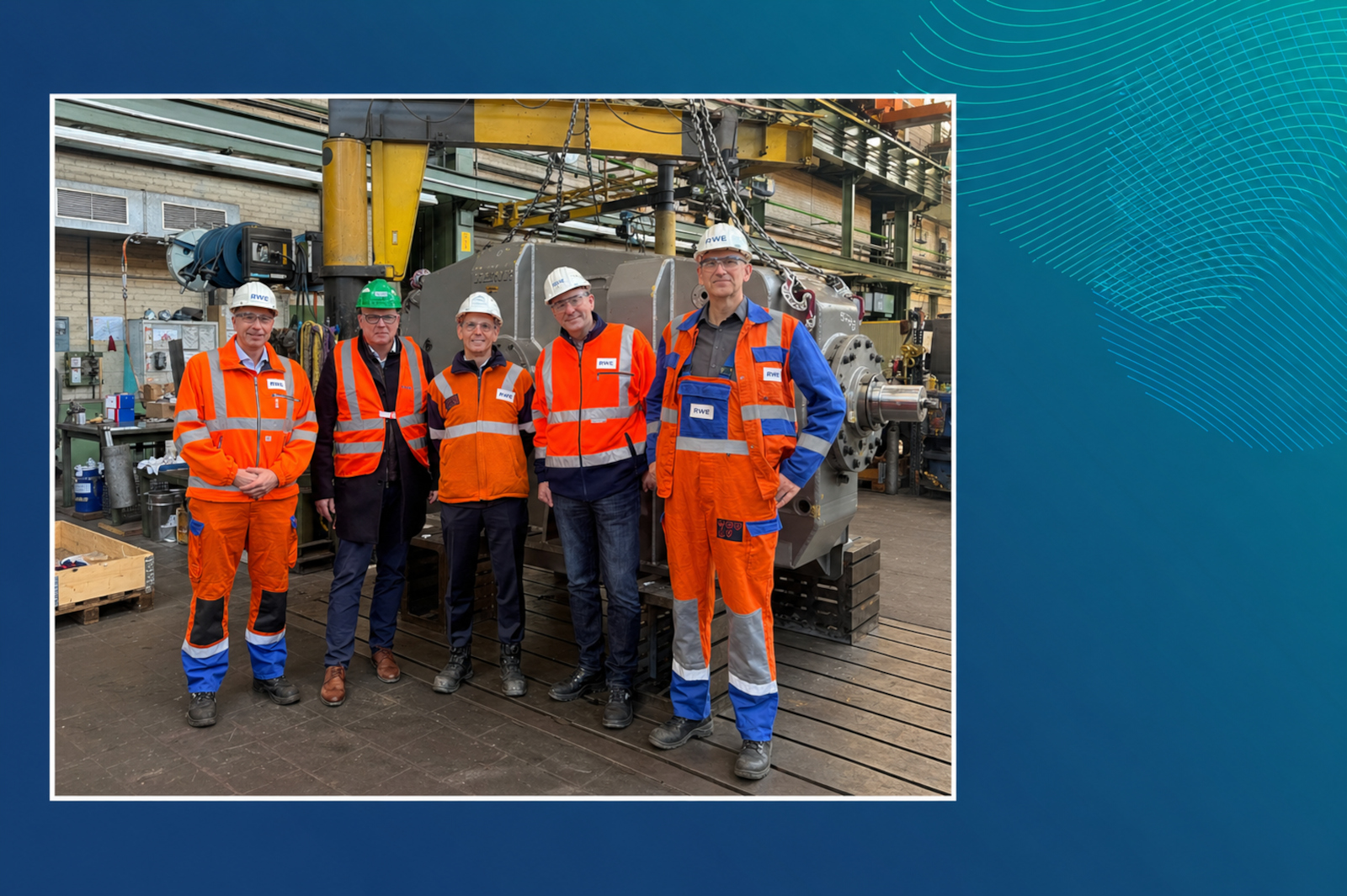 Fünf Arbeiter in weißen und grünen Schutzhelmen sowie leuchtend orangefarbenen Warnanzügen und Westen stehen vor einer schweren Maschine und einem gelben Hallenkran in einer Industriehalle.
