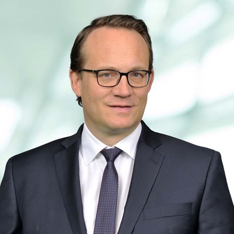 Ein Mann in einem dunklen Anzug und einer Krawatte steht vor einem verschwommenen Hintergrund und vermittelt ein professionelles Erscheinungsbild, Portrait von Dr. Markus Krebber.