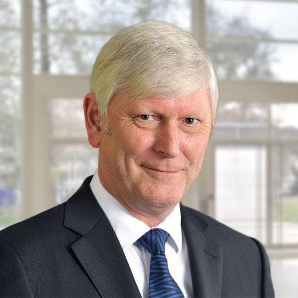 Ein Mann in einem Anzug mit hellblondem Haar steht vor einem Fenster mit unscharfem Hintergrund, Portrait von Dr. Rolf Martin Schmitz.