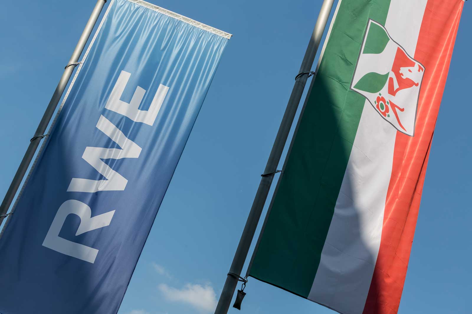 Two flags flutter in the wind, a blue one with 'RWE' and a green, red, and white flag featuring a coat of arms.