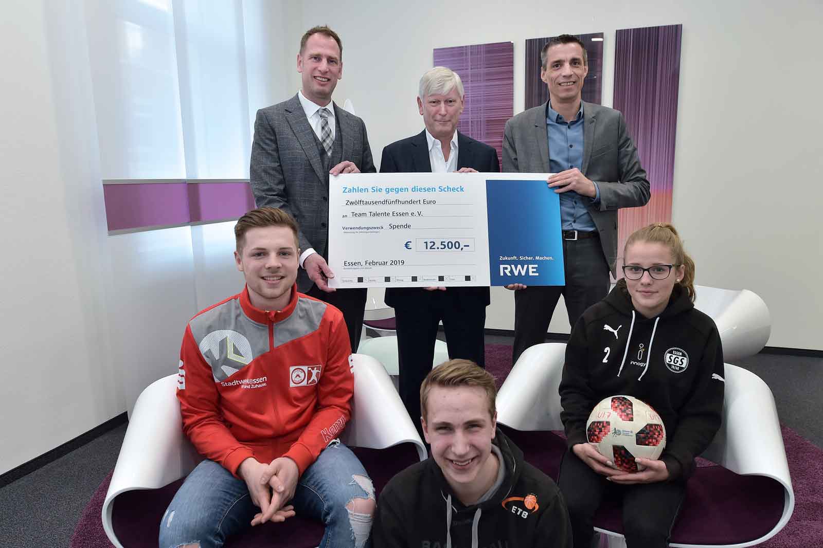 Eine Gruppe von Personen mit einem großen Scheck für Team Talente Essen e.V., dargestellt in einem modernen Raum.