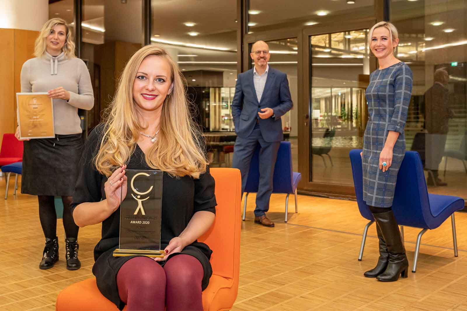 Eine Gruppe von Menschen in einer modernen Umgebung, die Auszeichnungen halten. Eine Person hält einen Preis, während andere zuschauen.