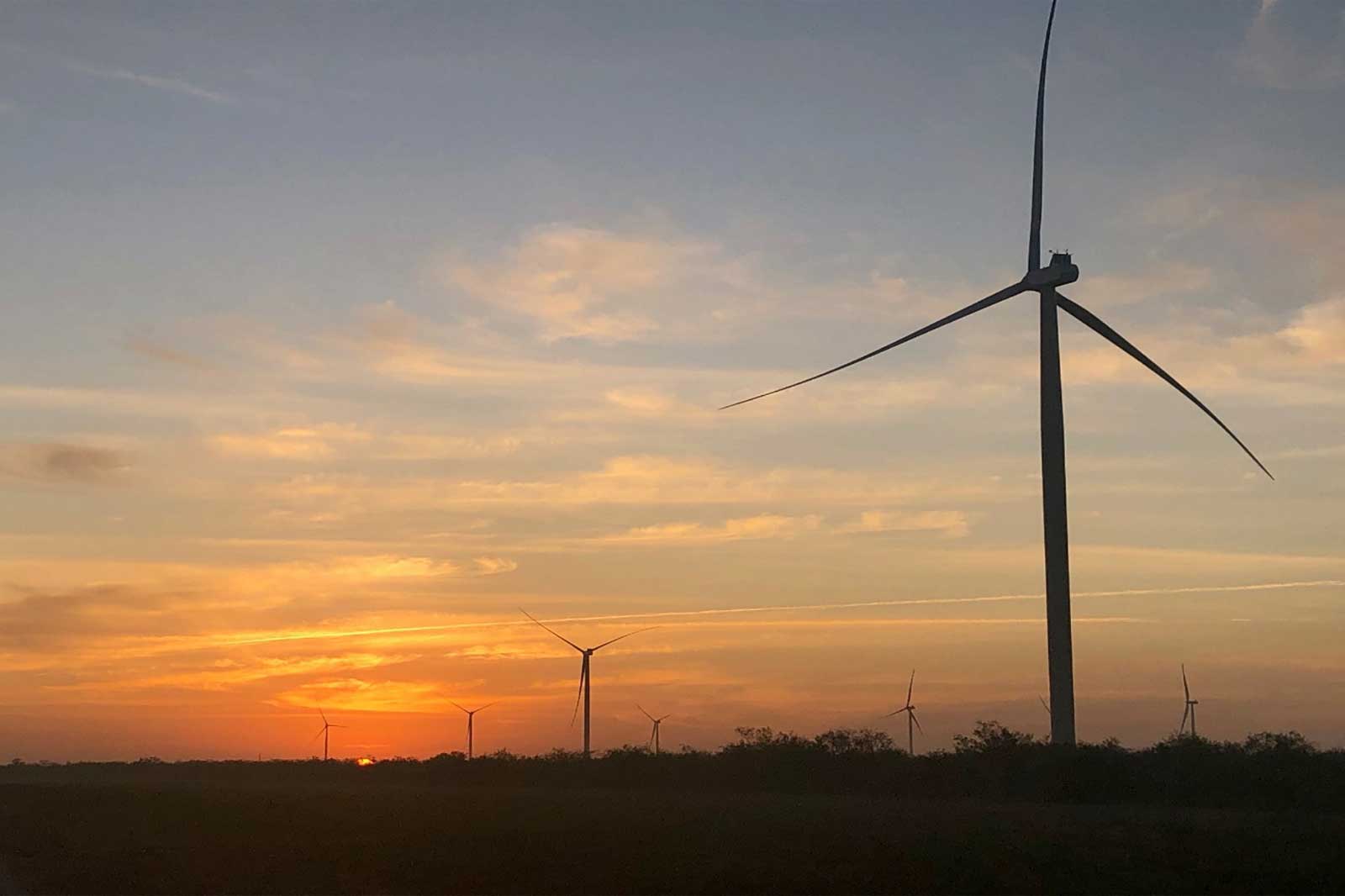 Ein Landschaftsbild von Windkraftanlagen vor einem Sonnenuntergang, das erneuerbare Energie in einer ruhigen Umgebung hervorhebt.