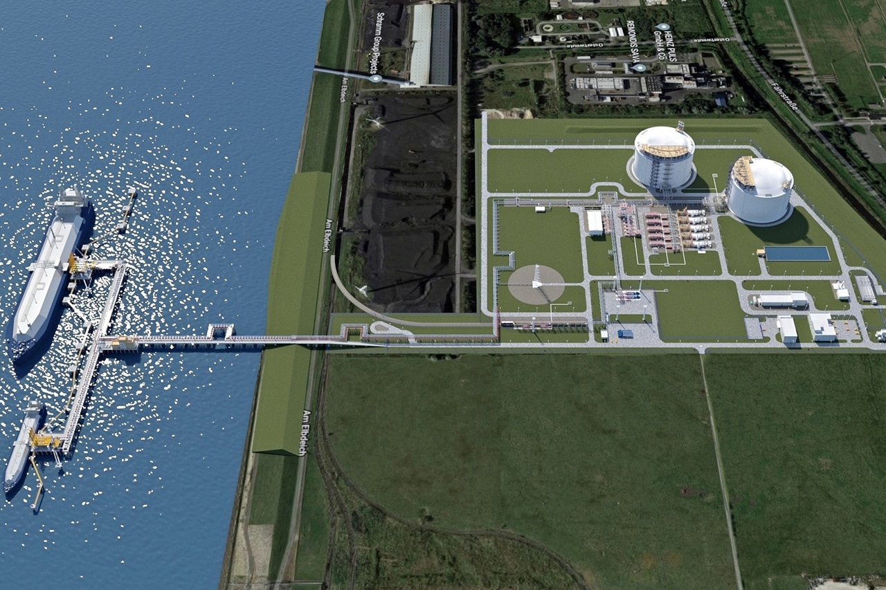 Aerial view of an LNG facility featuring a ship, pipelines, and large storage tanks by the water.