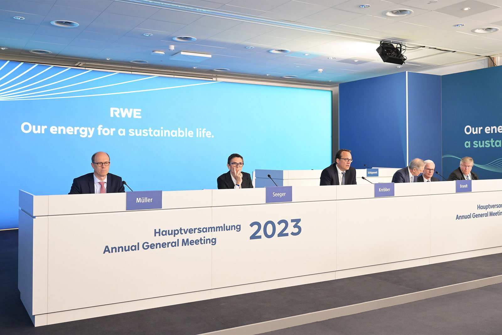 Die Bühne mit dem RWE-Schild und den Männern während der Hauptversammlung 2023, die alle auf ihre Papiere schauen.