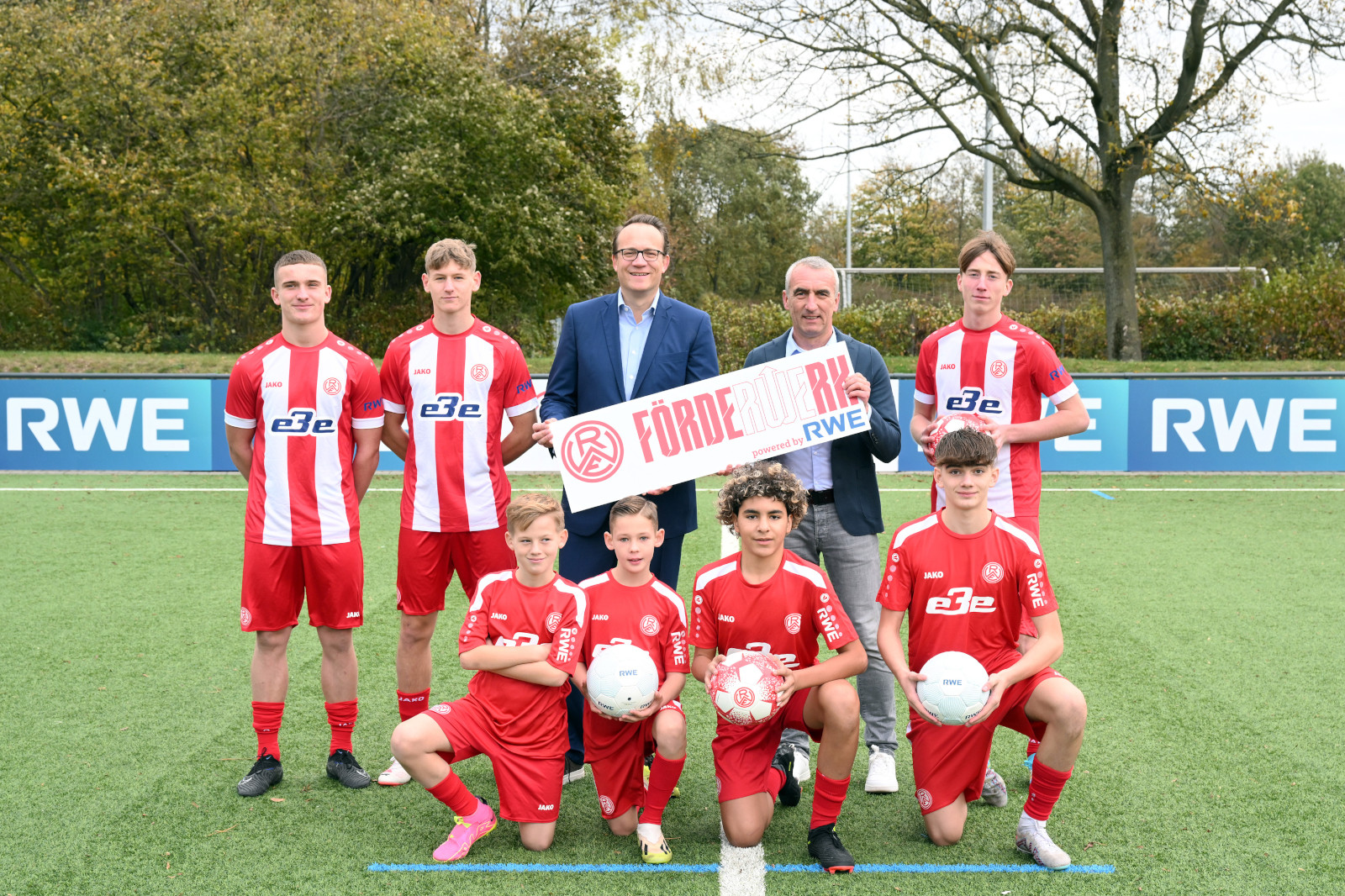 Eine Gruppe junger Fußballspieler in roten Trikots posiert mit einem Schild auf dem Platz und zeigt Teamgeist.