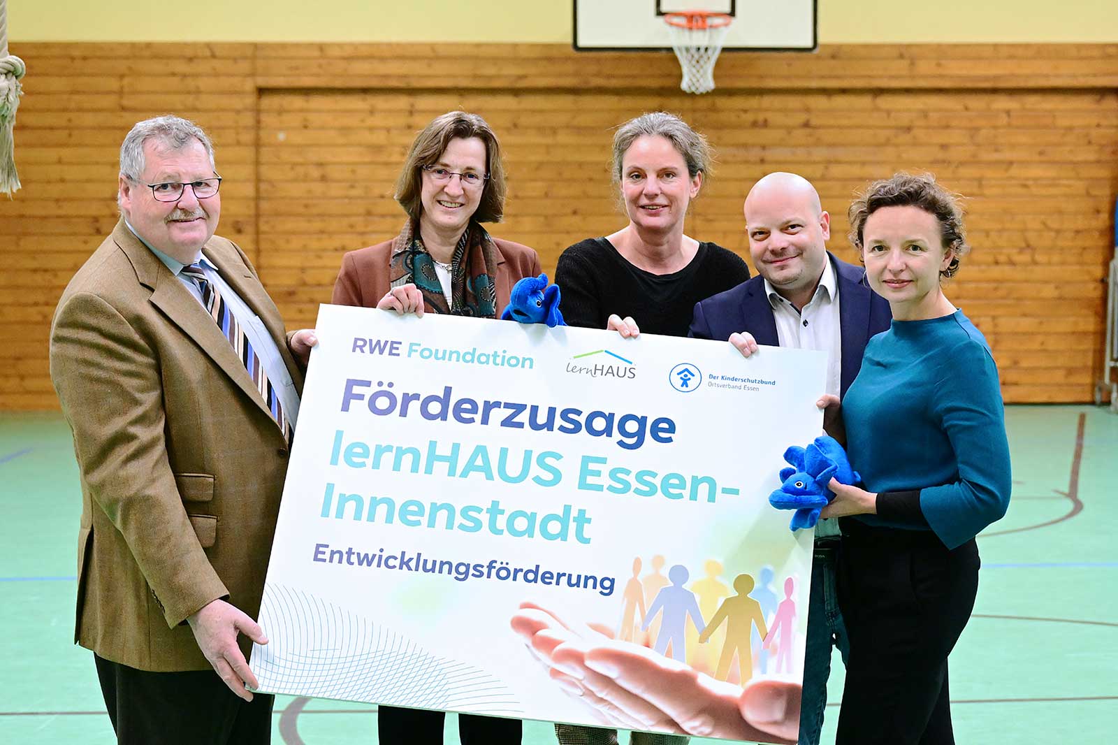 Group photo holding a large funding announcement for lernHAUS Essen-Innenstadt and a blue plush toy.