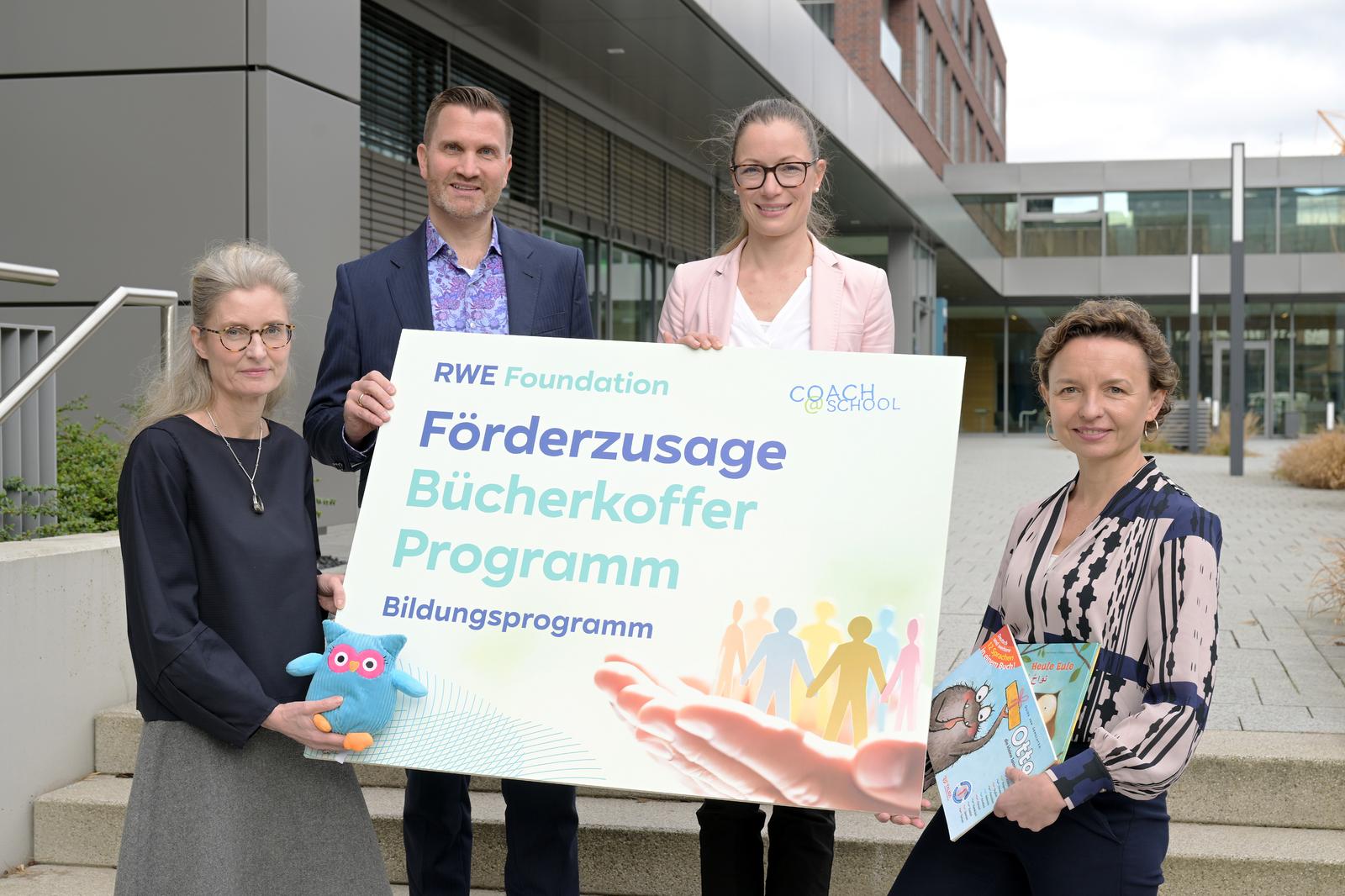 Vier Personen halten ein großes Schild für ein Bildungsprogramm der RWE Stiftung, umgeben von einem modernen Gebäude.