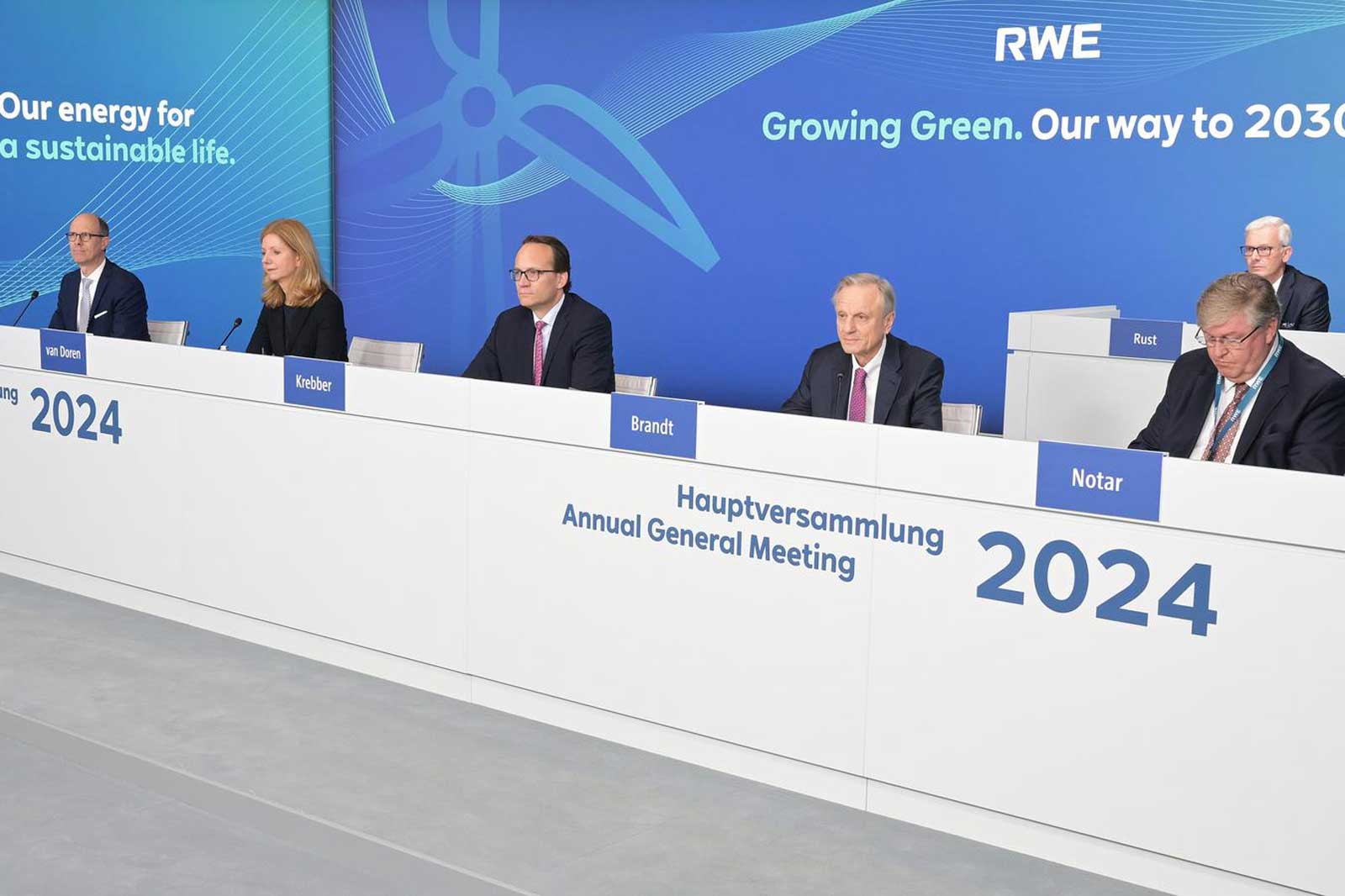 A group of individuals sits at a table during RWE's Annual General Meeting 2024. The company's logo is displayed behind them.
