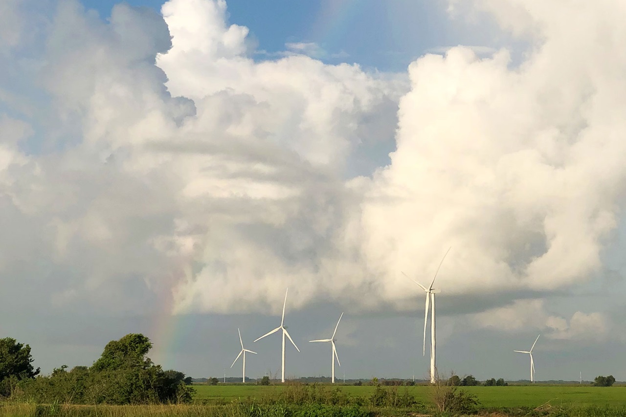 Fünf Windkraftanlagen stehen auf einem Feld, umgeben von Wolken und einem Regenbogen im Hintergrund.