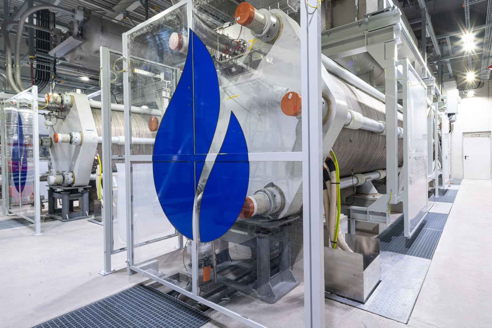 Ein industrieller Raum mit großer Maschine, die ein blaues Flammenlogo und transparente Paneele zeigt.