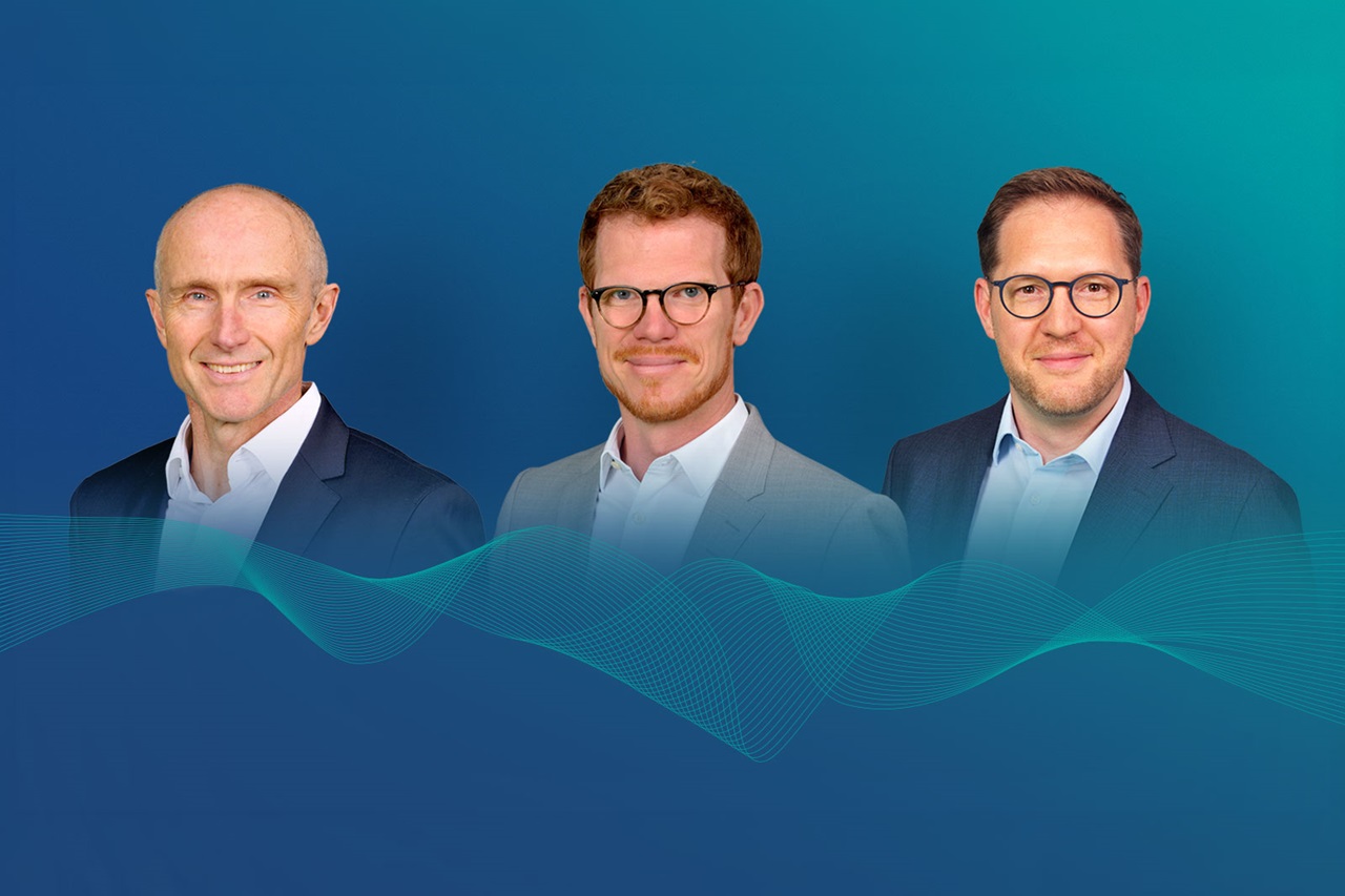Three men in business attire stand shoulder-high against a teal-to-blue gradient; two wear glasses, all smile above a translucent aqua waveform graphic.