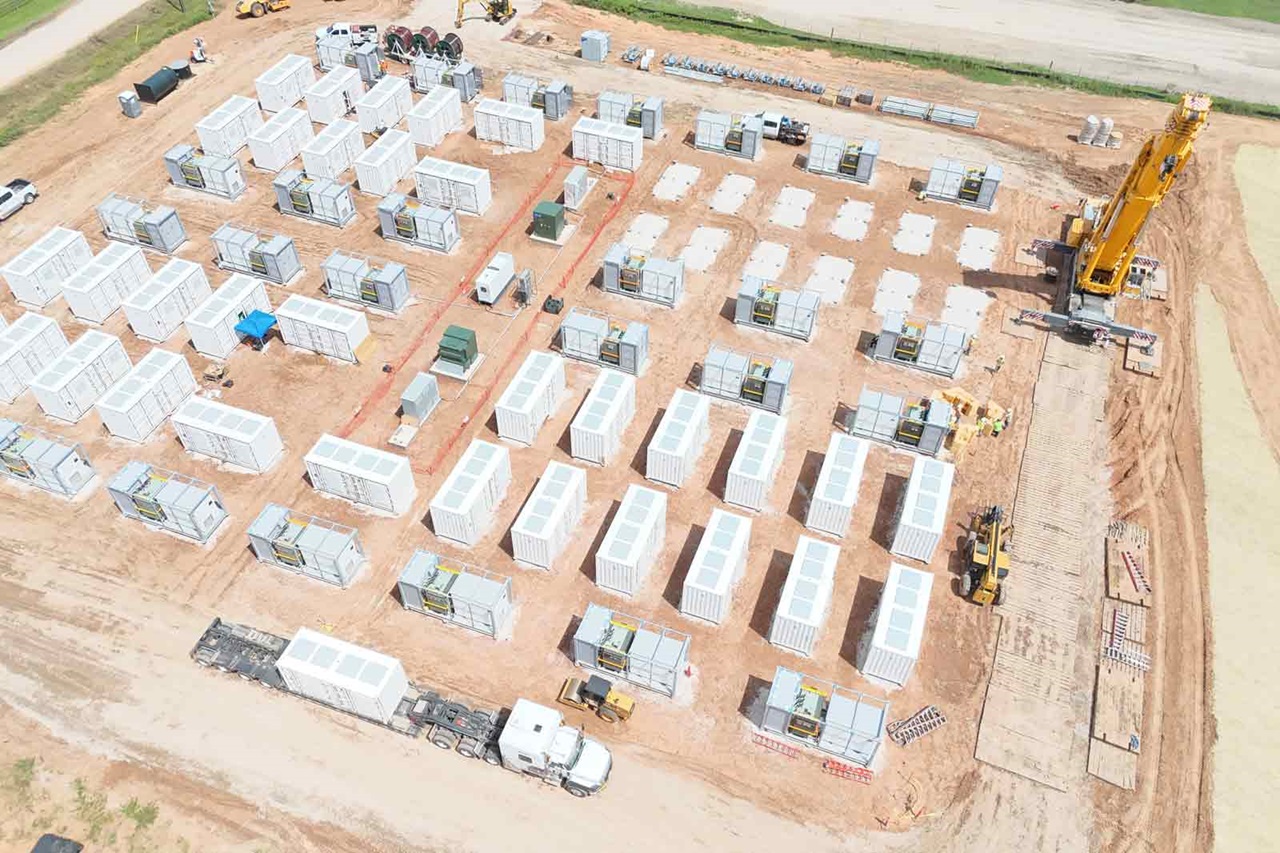Aerial view of a construction site with numerous energy storage containers, machinery, and a crane on the site.