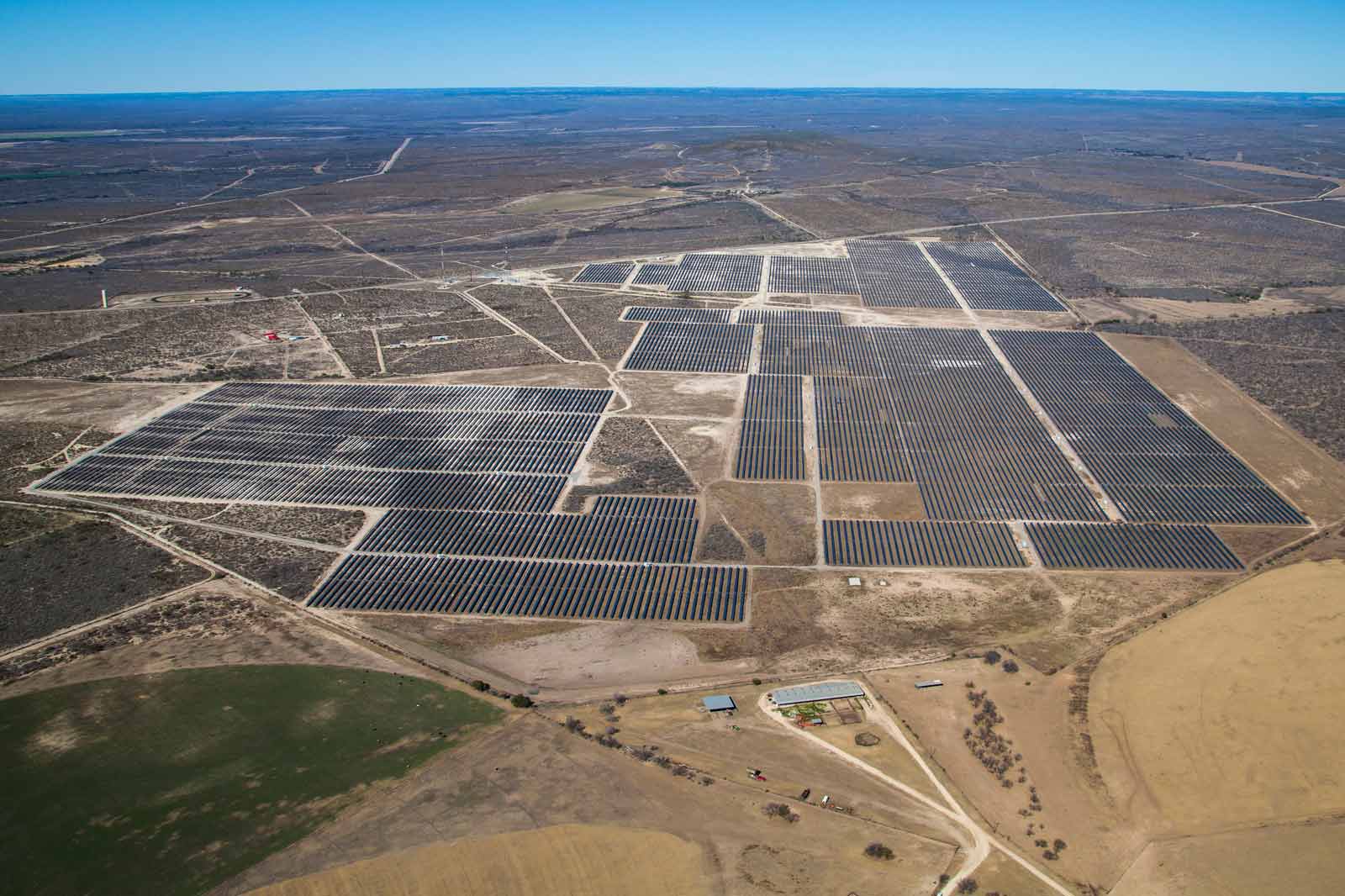 A large solar farm spans a vast landscape with numerous solar panels and wide fields in the background.