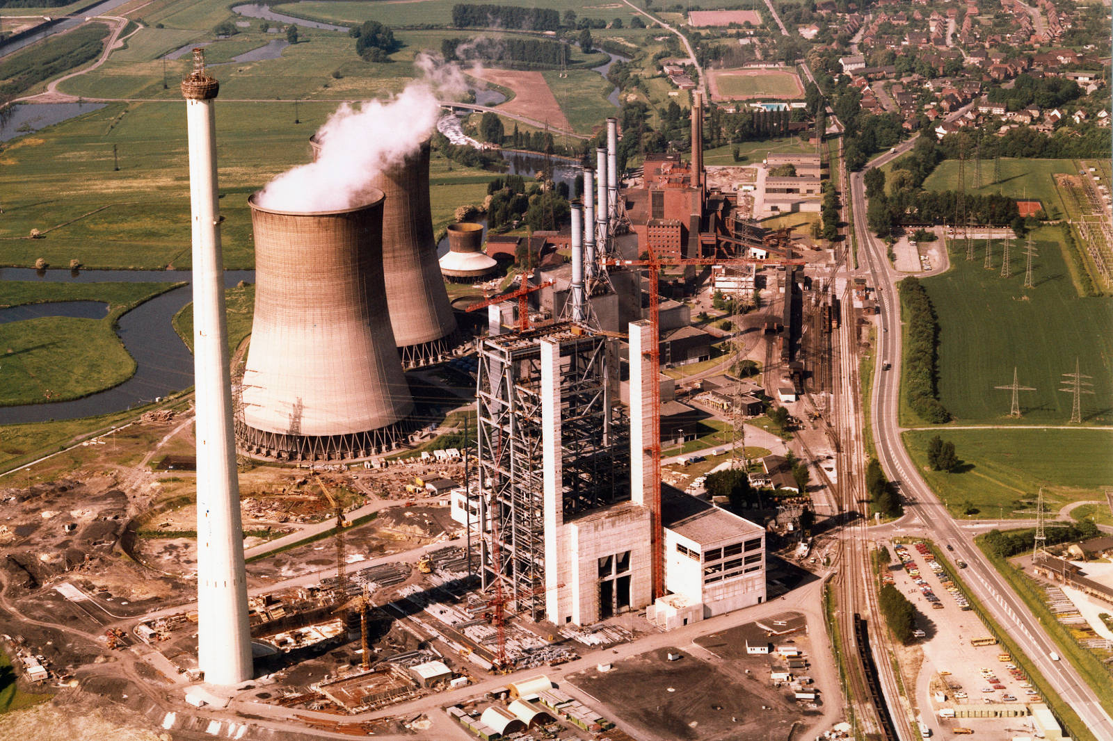 Eine Luftaufnahme eines Kraftwerks mit Kühltürmen und einer großen Industrieanlage, umgeben von grünen Feldern.