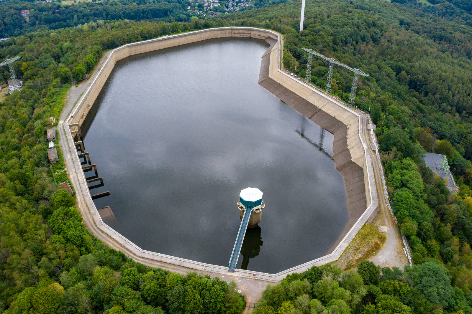 Eine Luftaufnahme eines großen Reservoirs, umgeben von grünen Bäumen, mit einem zentralen Turm und einem Zugangsweg.