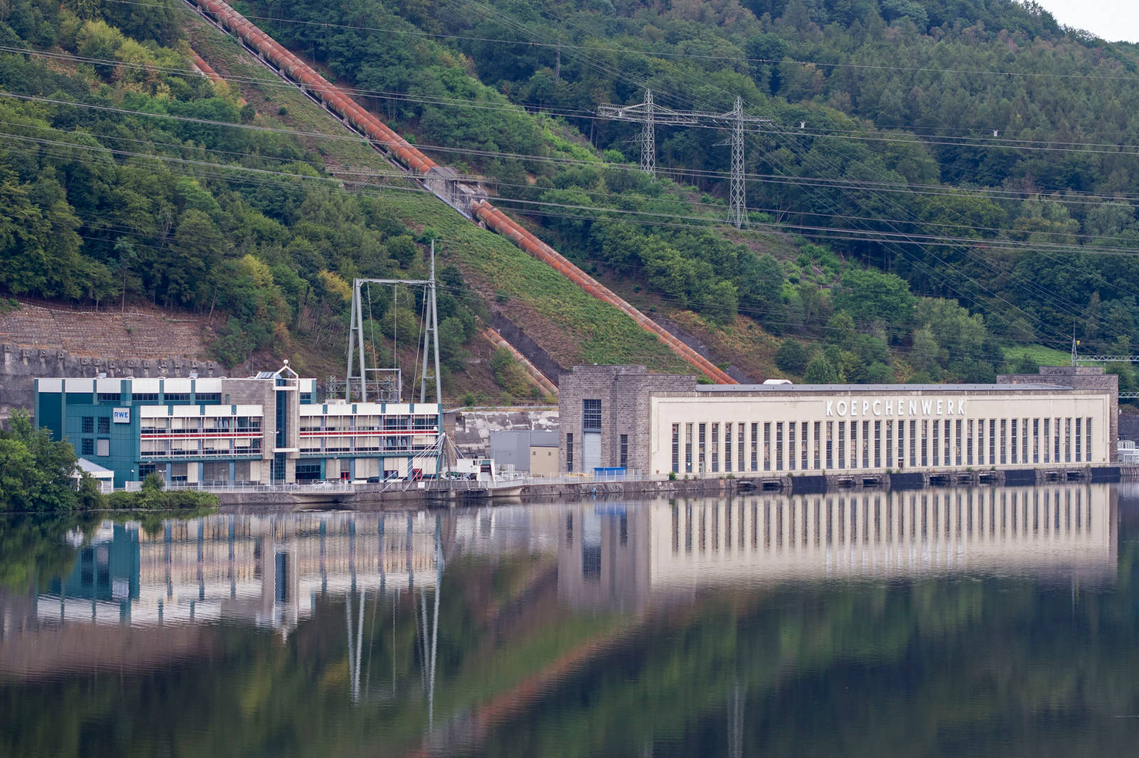 Das Koeppchenwerk am Fluss spiegelt den bewaldeten Hügel mit Rohren wider, die den Hang hinaufführen.