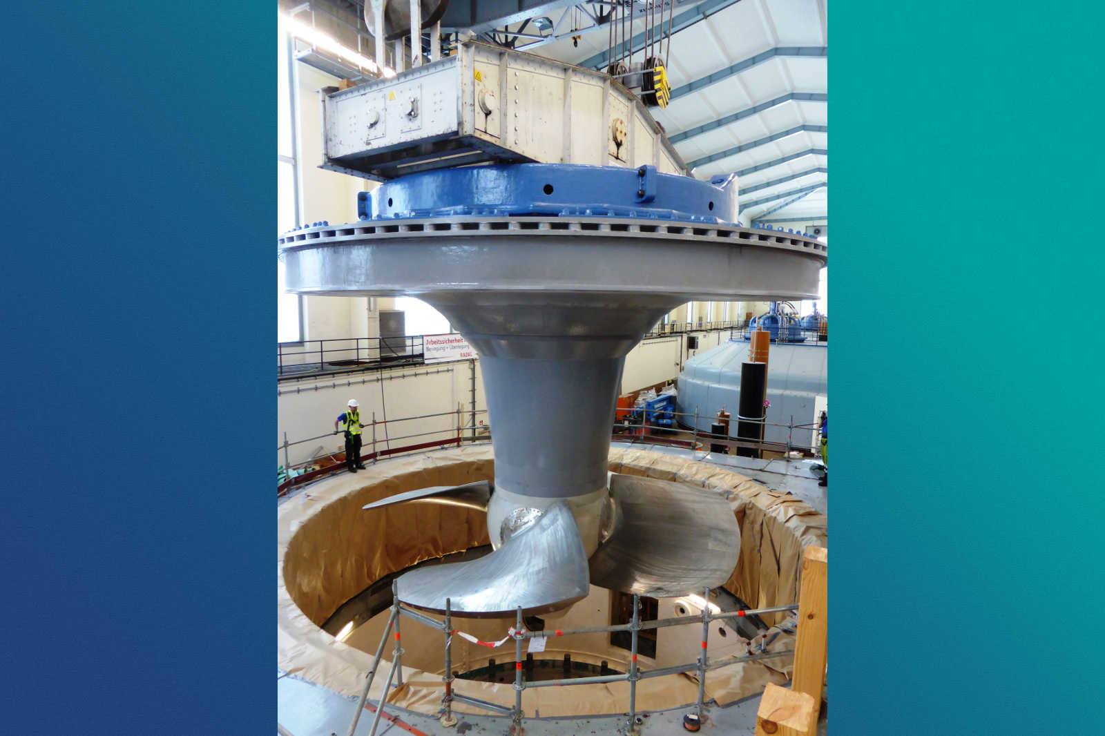 Eine große Turbine wird in einer Fabrik montiert, mit sichtbaren Arbeitern und Geräten.