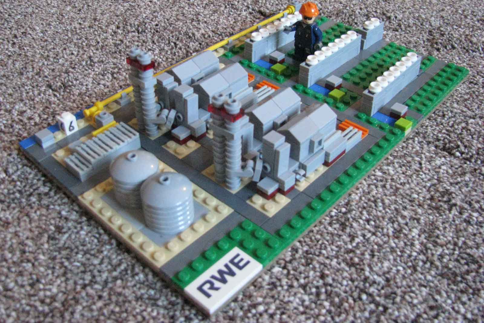 A Lego construction depicting a power plant with grey structures, tanks, and a figure near a control area.