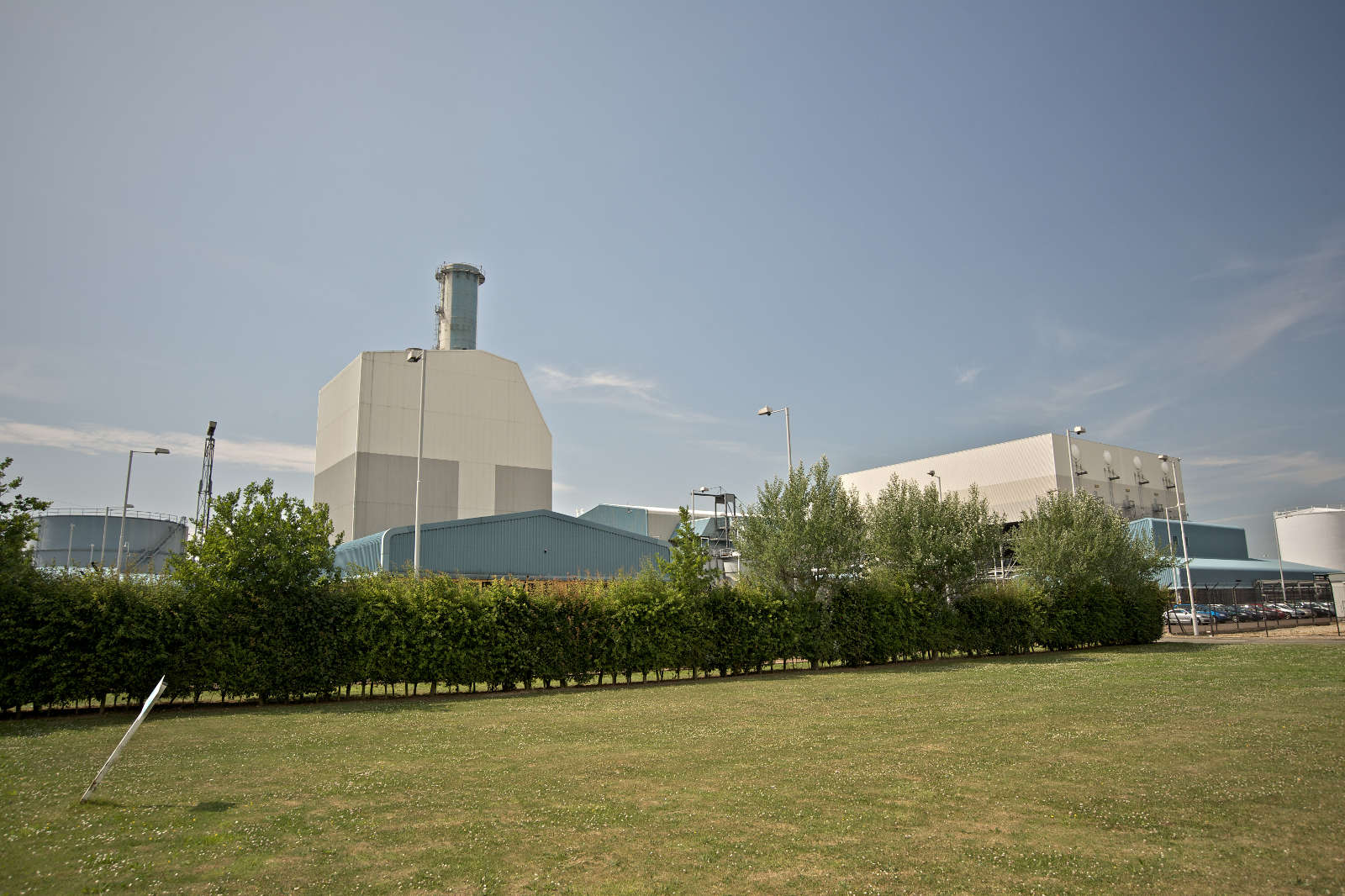 A modern industrial facility with large buildings, surrounded by greenery and a clear blue sky.