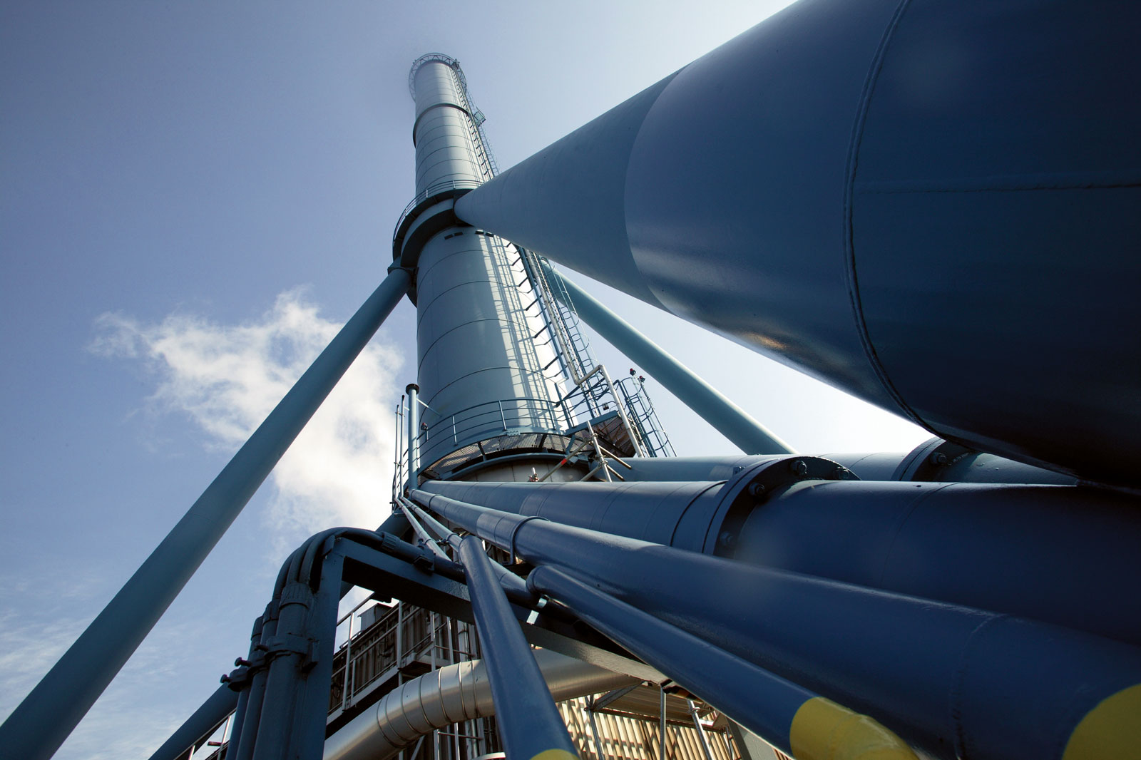 Eine Nahaufnahme einer hohen industriellen Struktur mit blauen Rohren und Treppen vor einem klaren Himmel.