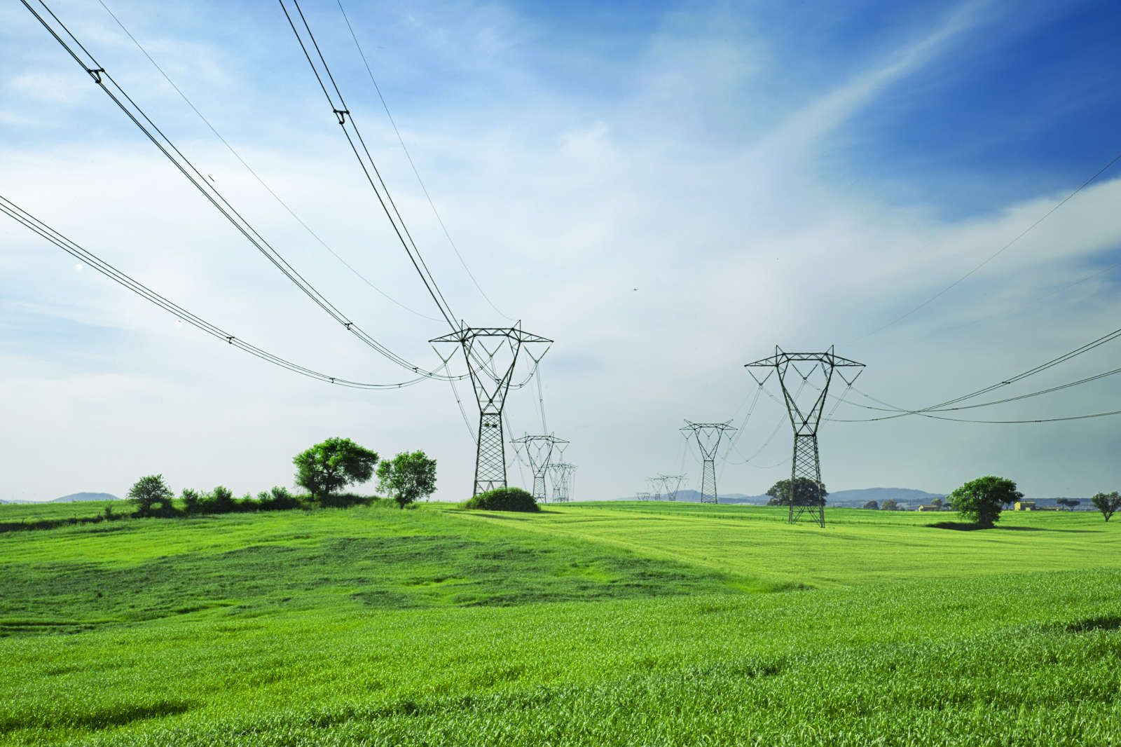 A landscape with green fields and power lines stretching across the horizon under a blue sky.