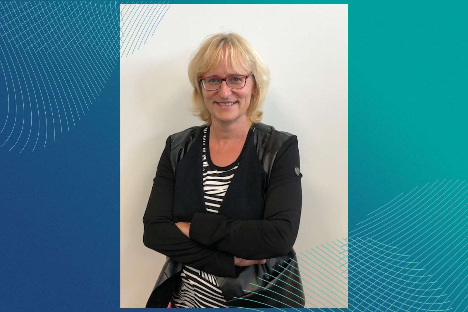 Eine Frau steht mit verschränkten Armen, trägt eine schwarze Jacke über einem gestreiften Oberteil, vor einem farbenfrohen Hintergrund.