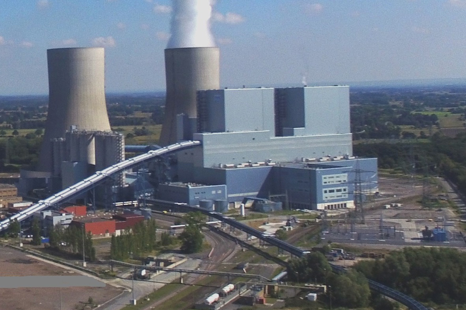 The image depicts a power station with two cooling towers and large facilities. Steam is rising, with visible landscape in the background.