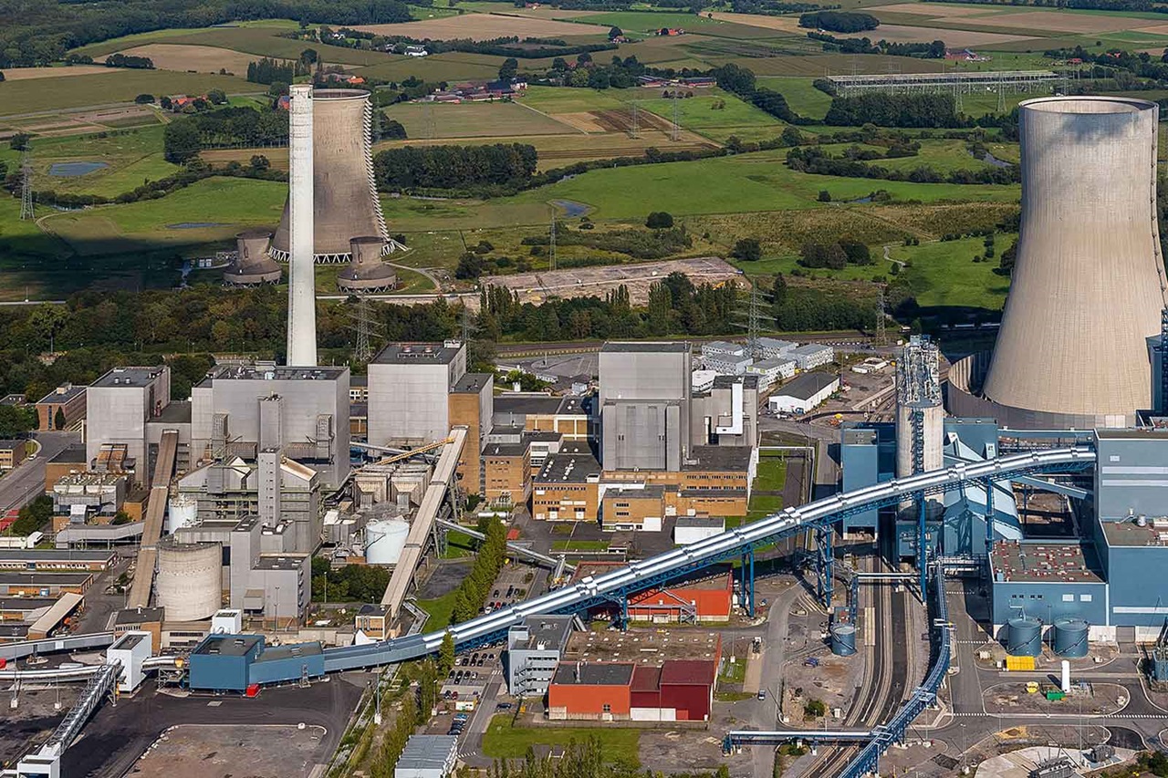 Luftaufnahme eines großen Industriekomplexes mit Kühltürmen, mehreren Gebäuden und umliegenden grünen Feldern.