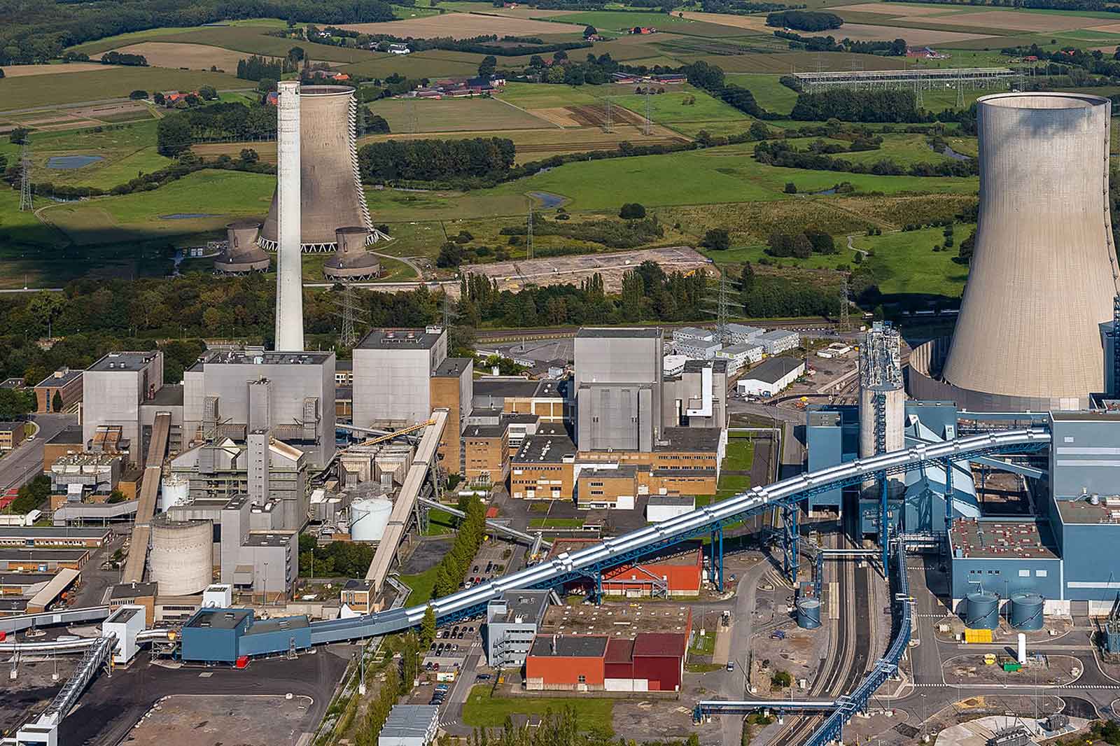 Luftaufnahme eines großen Industriekomplexes mit Kühltürmen, mehreren Gebäuden und umliegenden grünen Feldern.