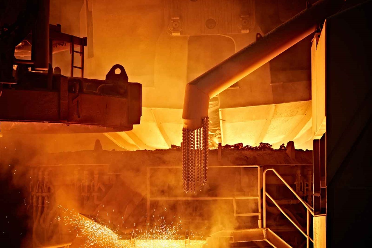 An industrial scene featuring molten metal, smoke, and sparks emanating from a furnace.