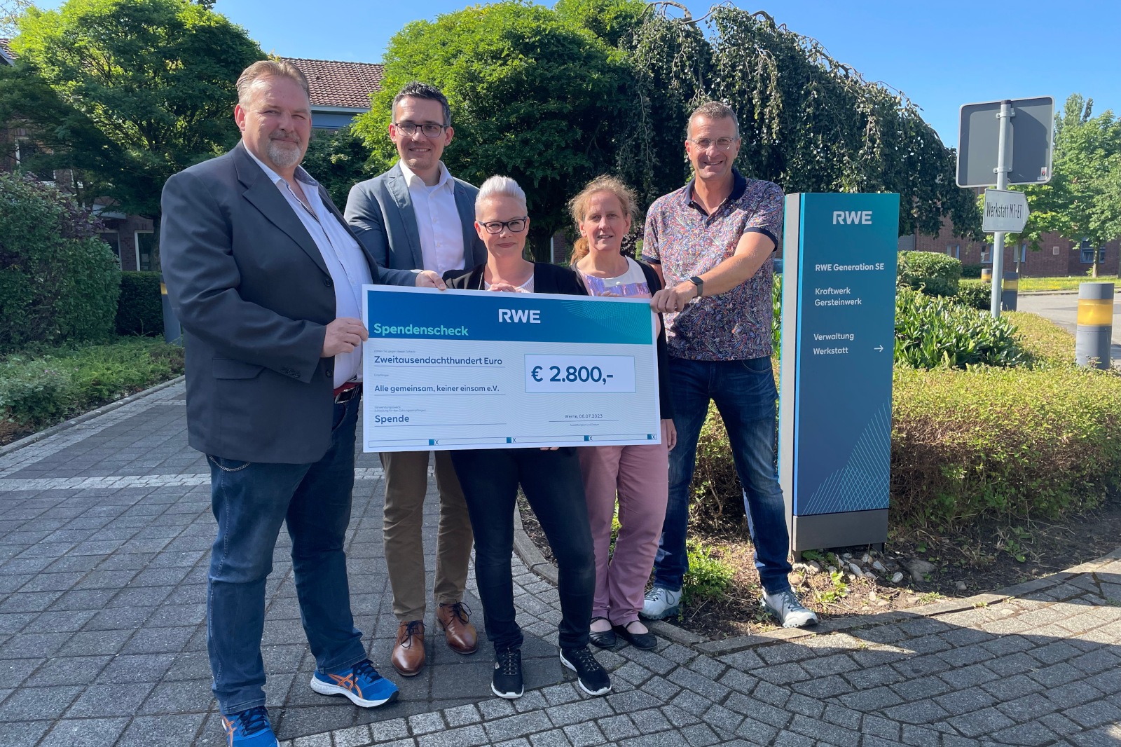 Eine Gruppe hält einen großen Scheck über 2.800 € vor einem RWE-Büro und feiert eine Spende.