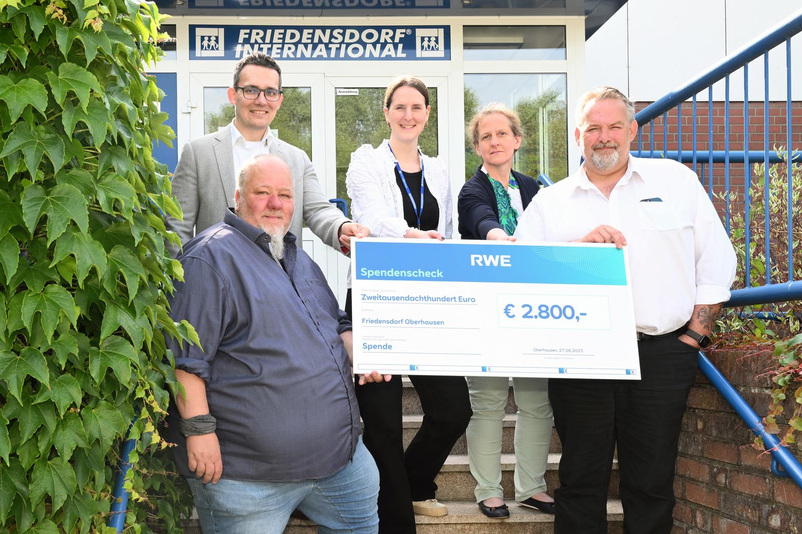 Eine Gruppe präsentiert einen großen Scheck über 2.800 € vor dem Friedensdorf International.