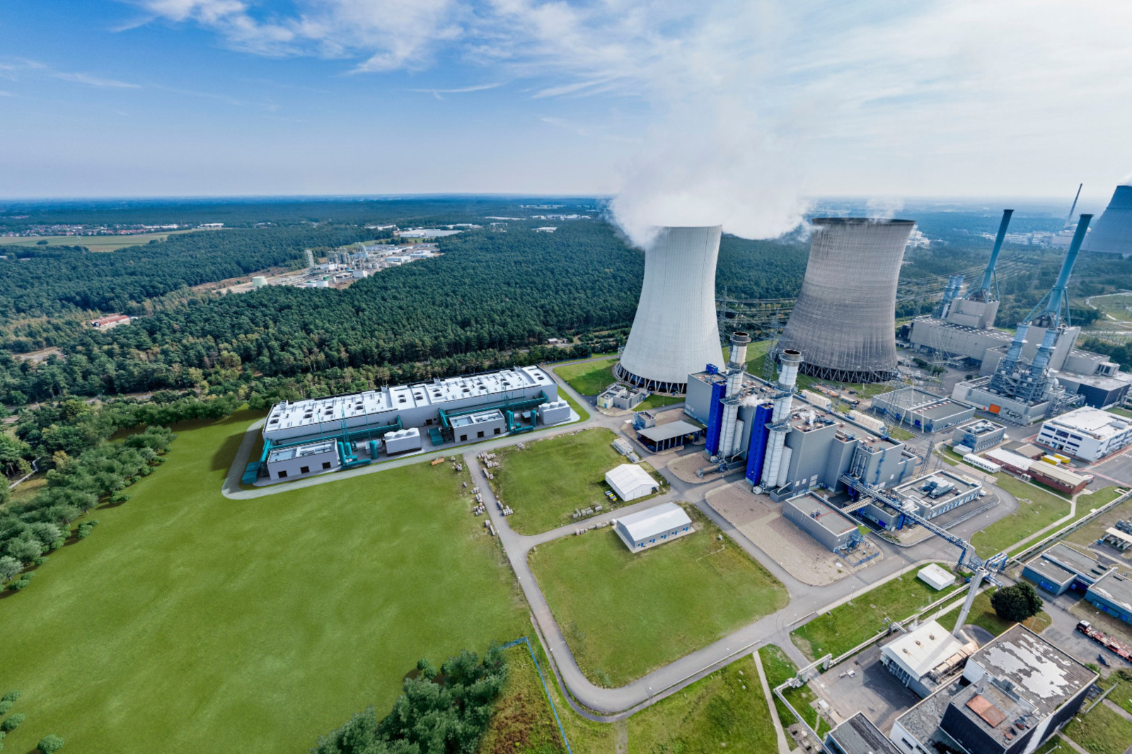 Luftaufnahme eines Kraftwerks mit Kühltürmen, Industriegebäuden und umgebender Begrünung unter klarem Himmel.