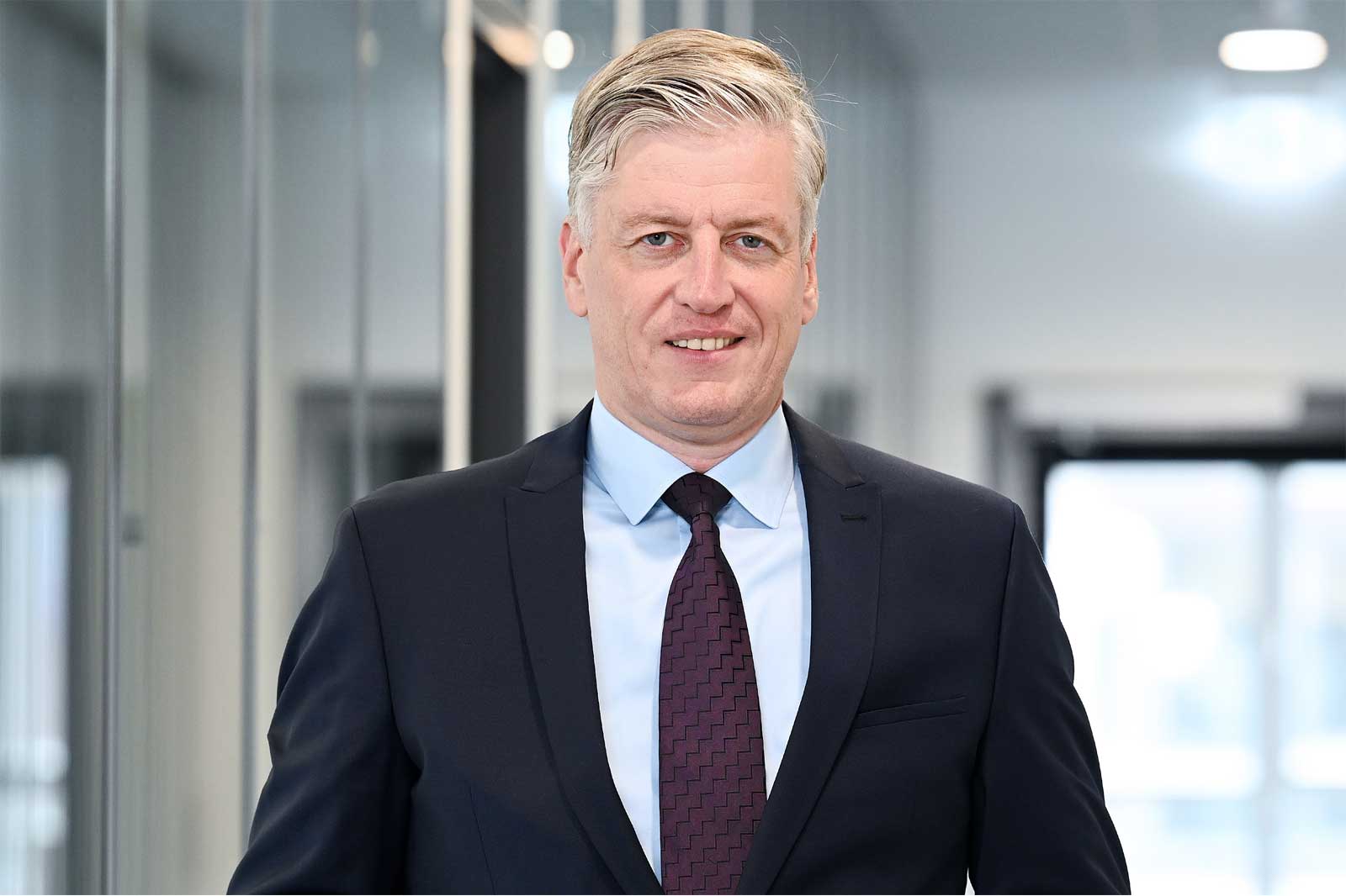 Ein Mann in formeller Kleidung steht in einem modernen Bür koridor, der Professionalität und Selbstvertrauen ausstrahlt.