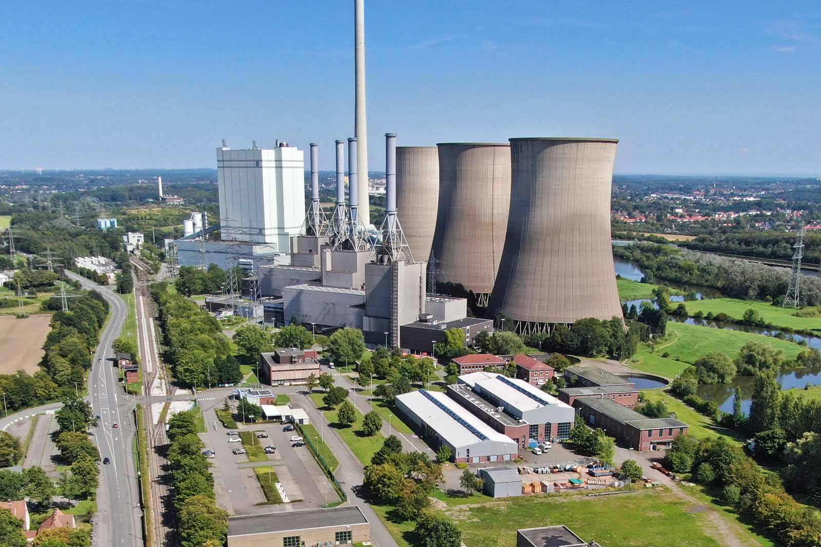 Eine Luftaufnahme eines Kraftwerks mit Kühltürmen, Industrieanlagen und angrünendem Grün entlang eines Flusses.