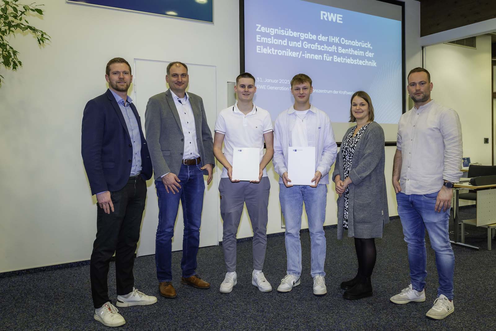 Eine Gruppe von Personen in Geschäftskleidung, die während einer Präsentationsveranstaltung bei der RWE Zertifikate halten.