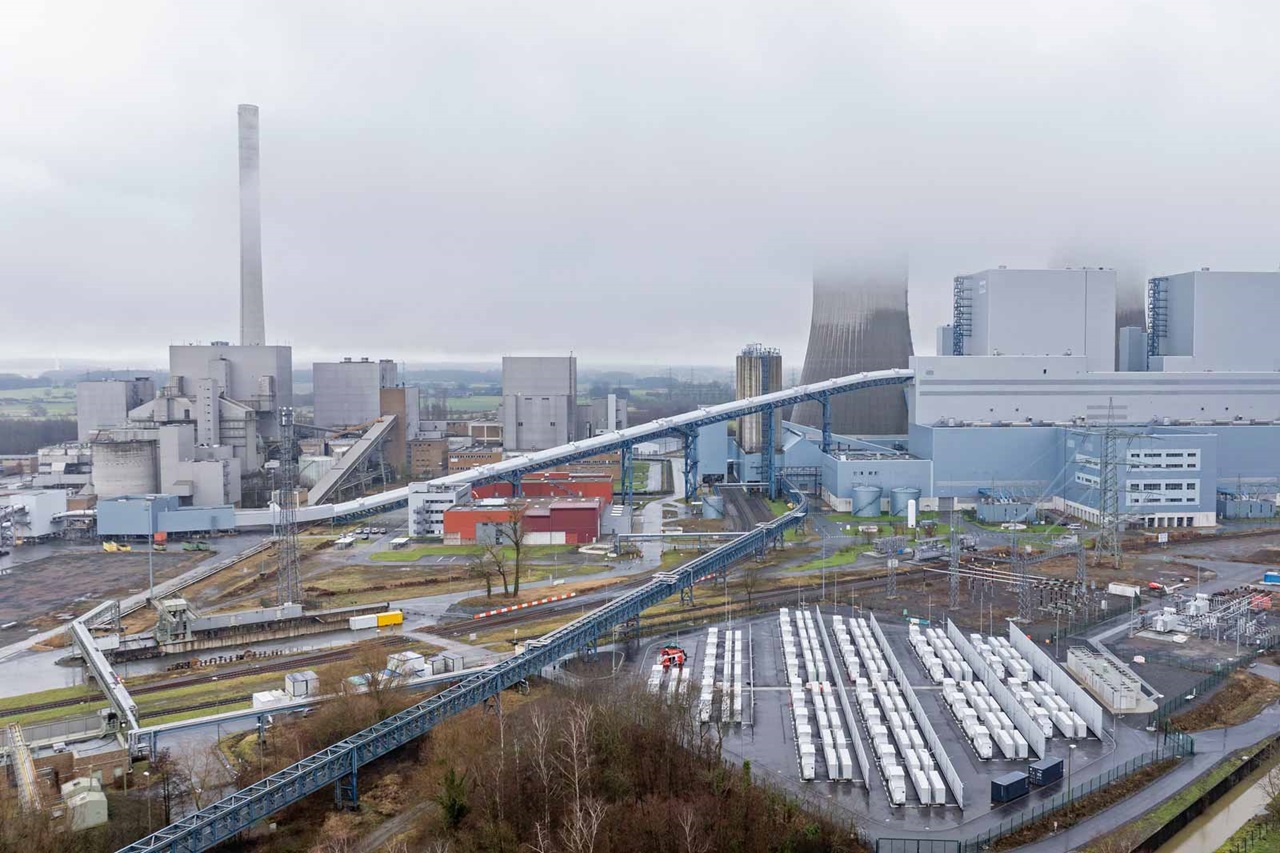 Eine Panoramaansicht eines Industriekomplexes mit Lagerhäusern, Förderbändern und einem hohen Schornstein, der im Nebel gehüllt ist.