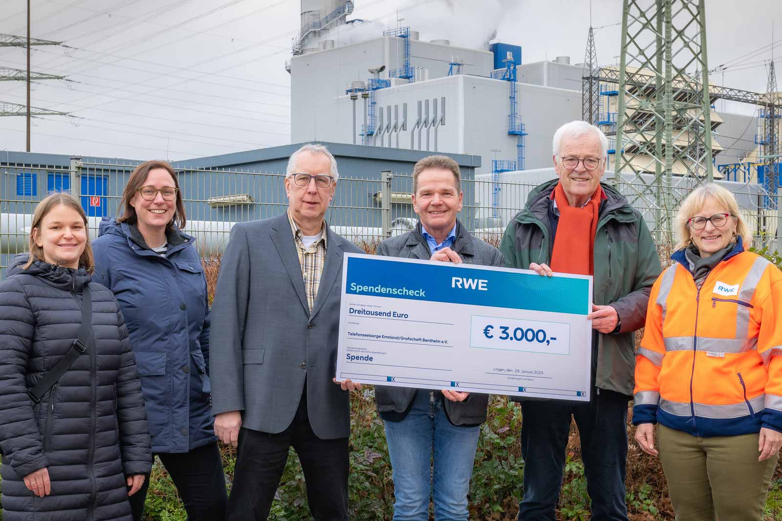 Eine Gruppe von Menschen hält einen großen Spendencheck über 3.000 € vor einem Industriegebäude.