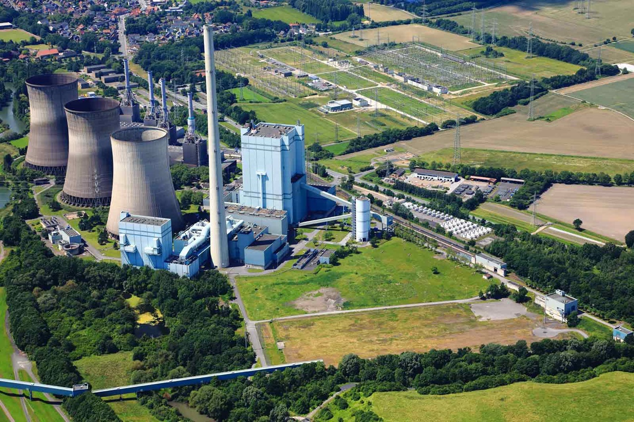 Eine Luftaufnahme eines Kraftwerks mit Kühltürmen, Industriegebäuden und grünen Feldern im Hintergrund.
