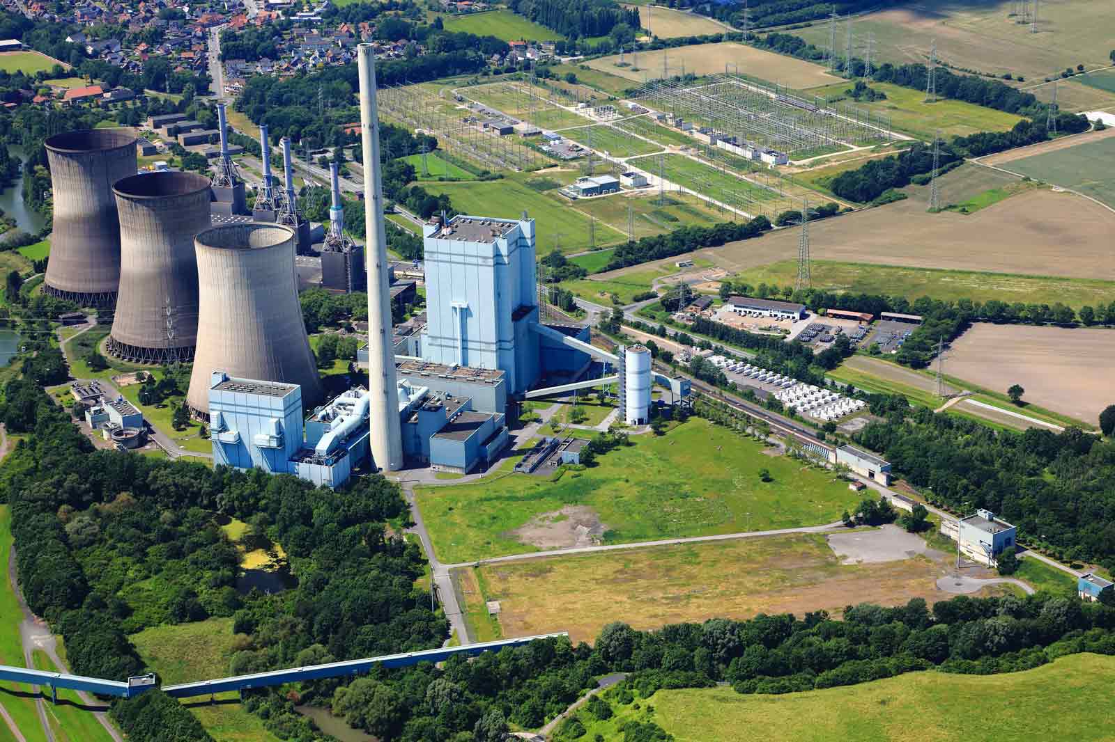 Eine Luftaufnahme eines Kraftwerks mit Kühltürmen, Industriegebäuden und grünen Feldern im Hintergrund.