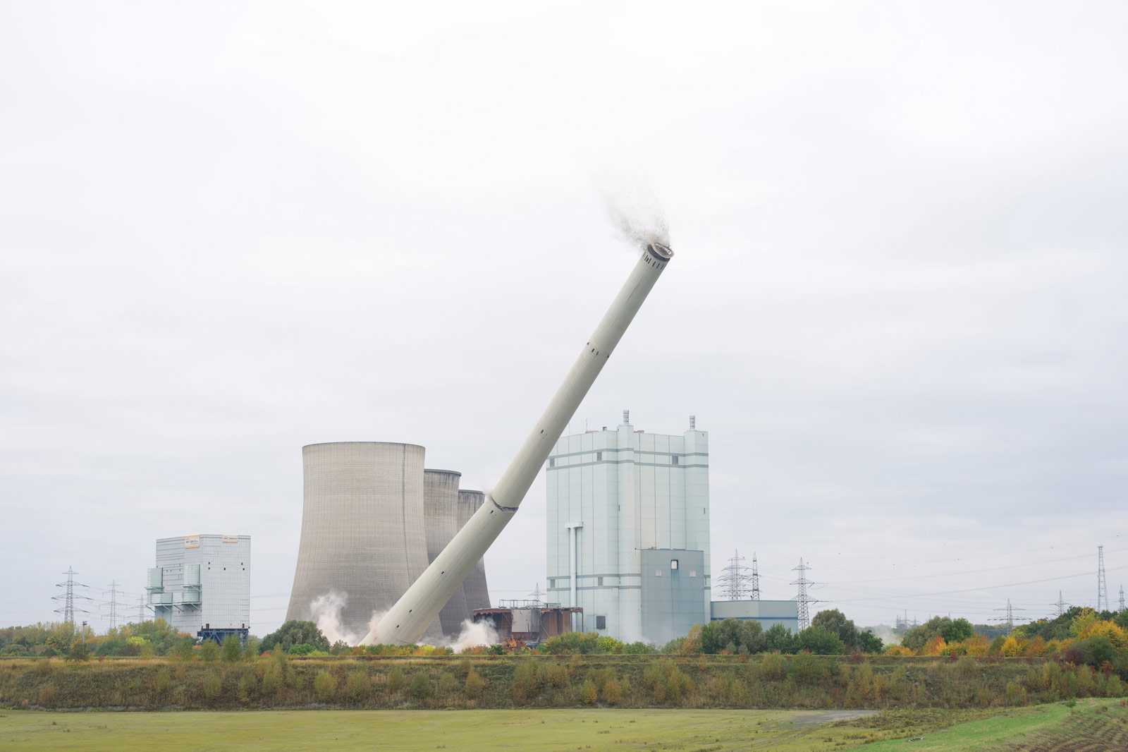 Ein schräg stehender Kühlturm kippt um, neben anderen Industriegebäuden unter einem bewölkten Himmel.