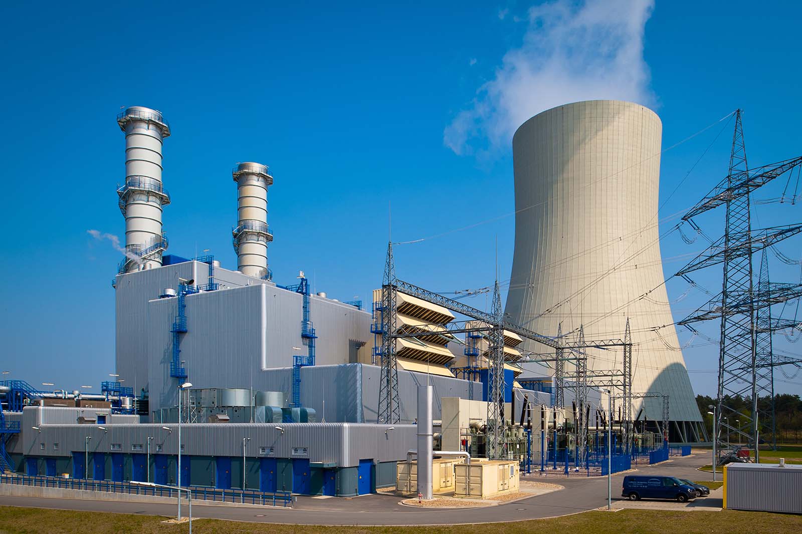 Kraftwerk mit großem Kühlturm zwei Schornsteinen Transformatoren und Strommasten.