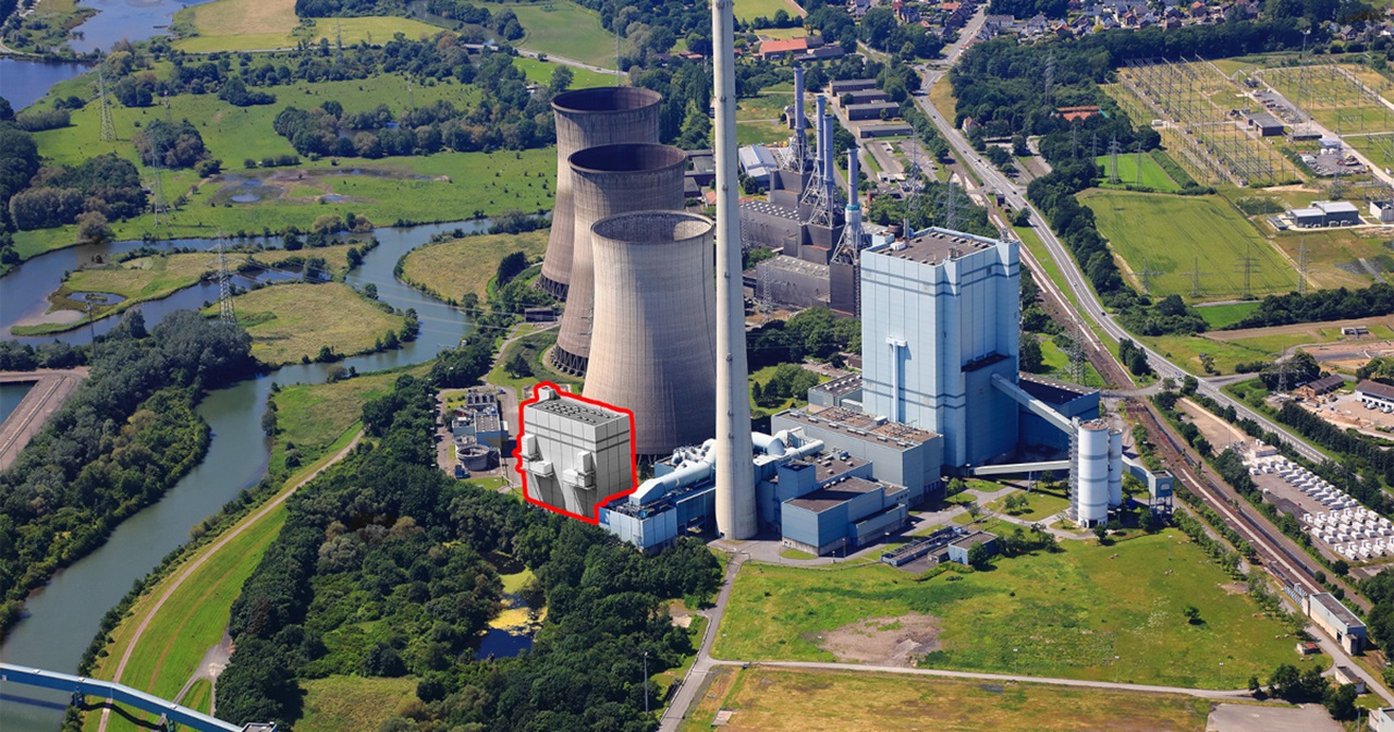 Luftaufnahme eines Kraftwerks mit Kühltürmen, einem hohen Schornstein und umliegendem Grün.